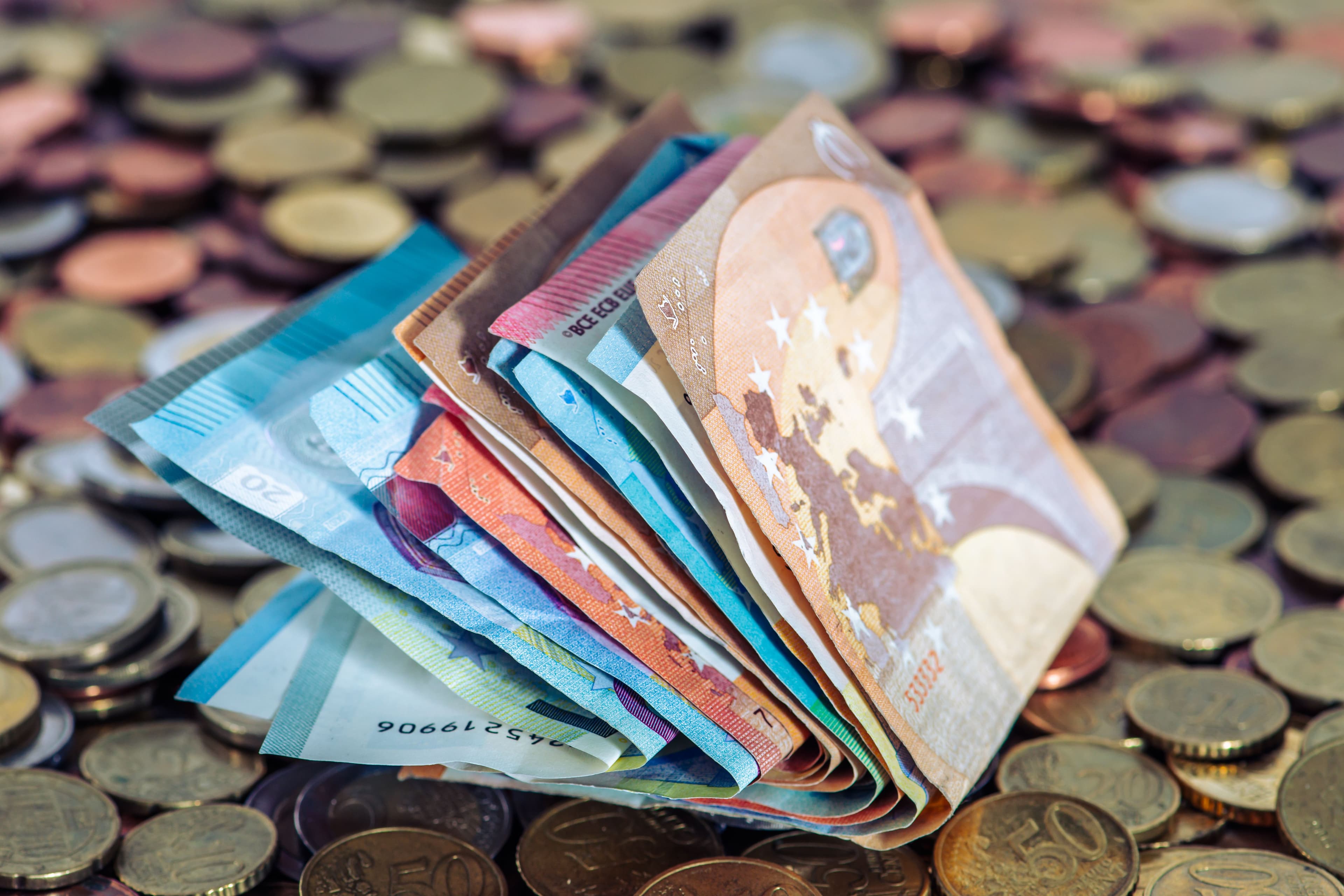 A stack of euro banknotes and scattered euro coins on a table